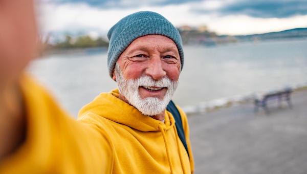 Un homme agé barbu et avec un bonnet faisant un selfie devant une plage bretonne
