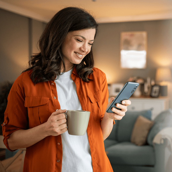Femme souriante tenant une tasse de café/thé en regardant son téléphone