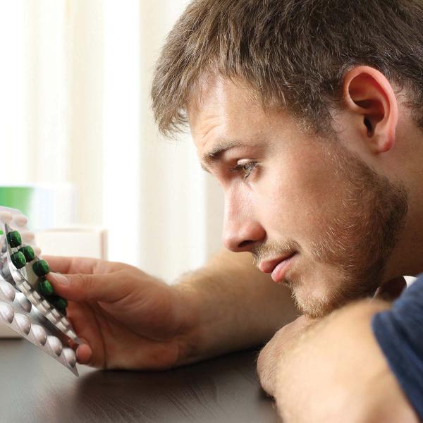 Jeune homme hésitant entre plusieurs plaquettes de cachets