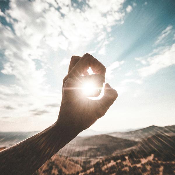 Soleil entre les doigts dressés vers le ciel
